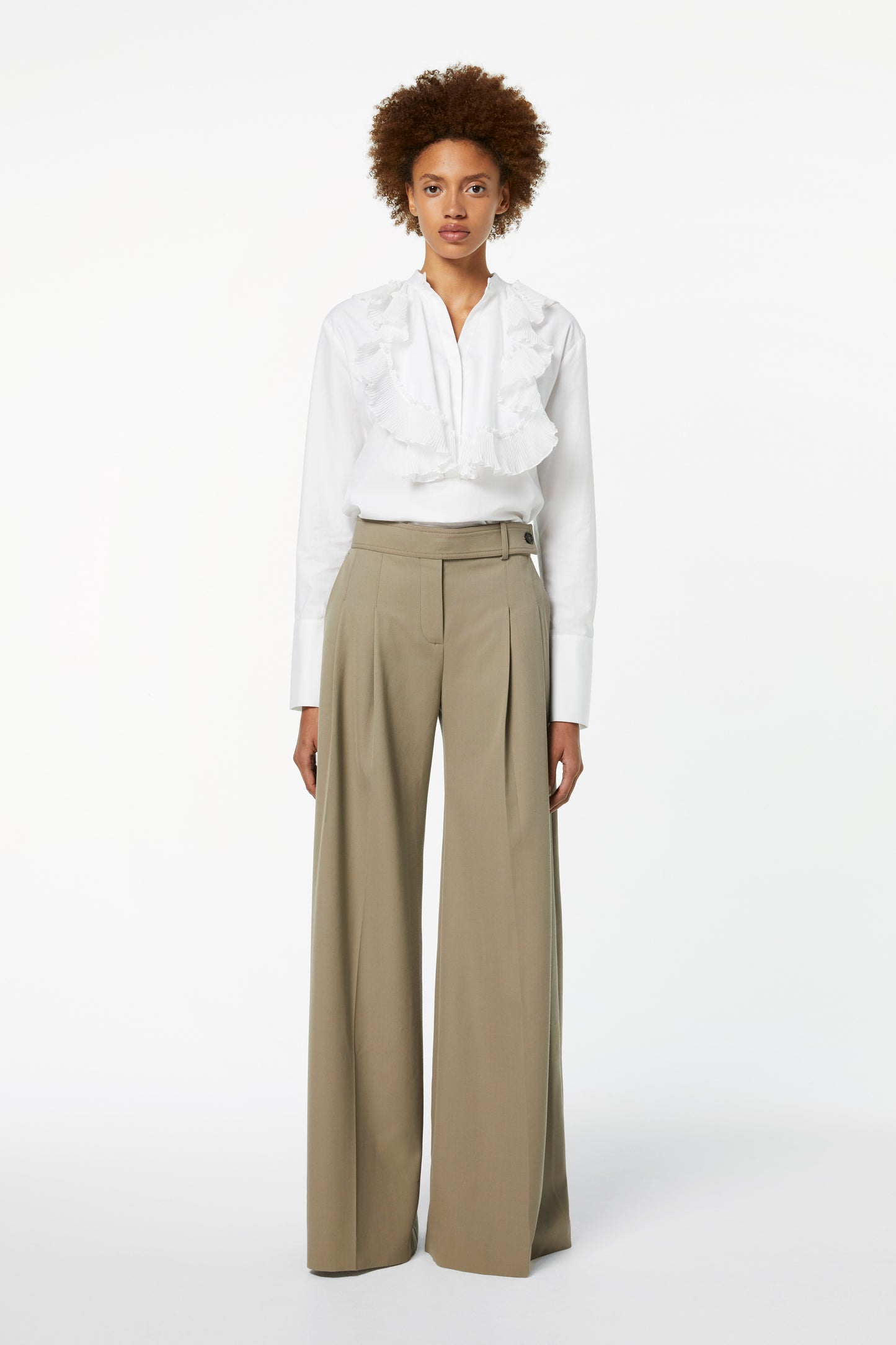 A person in a white ruffled blouse and Victoria Beckham's Wide-leg Trousers in Clay stands against a plain white background.
