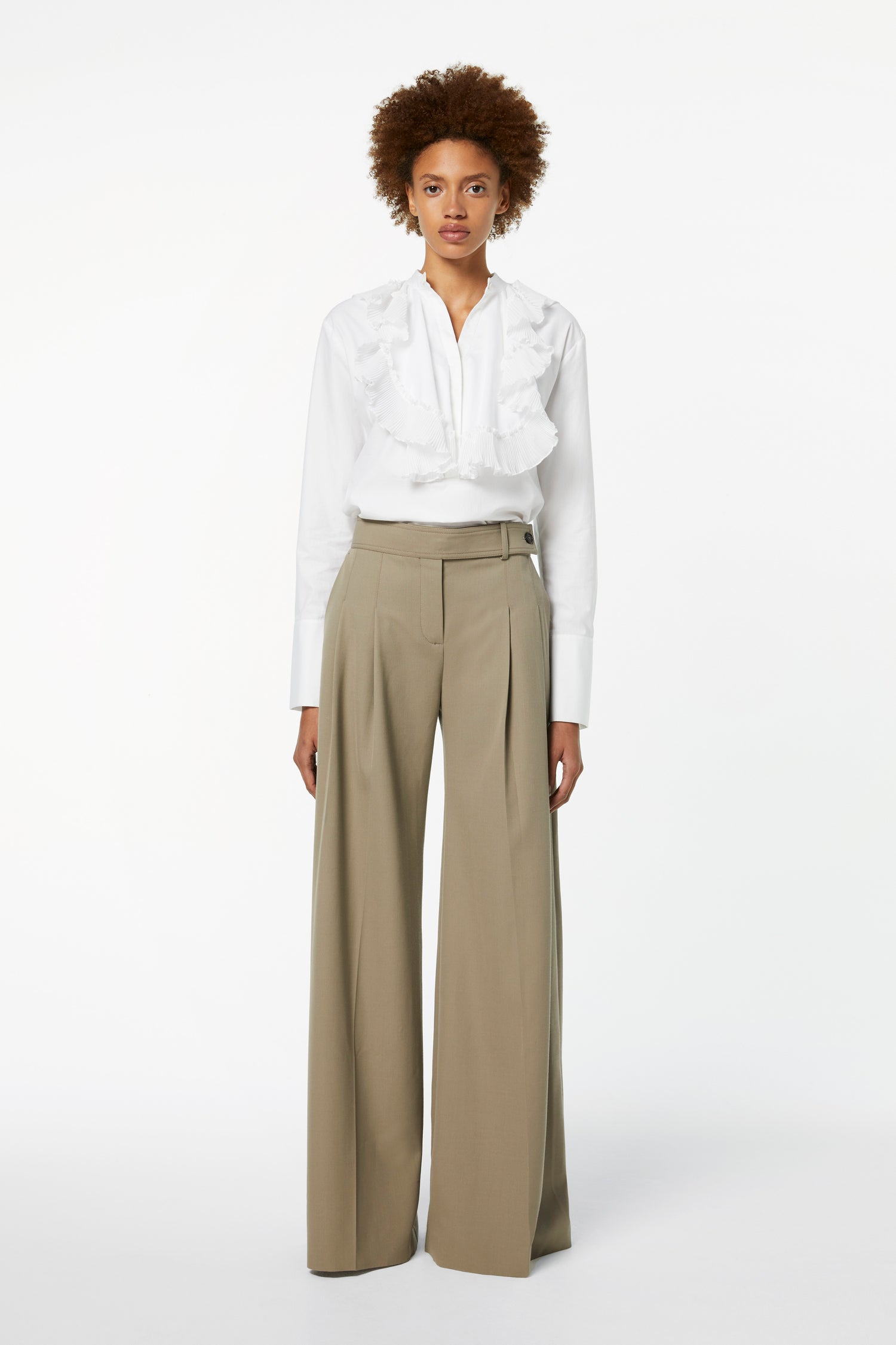 A person in a white ruffled blouse and Victoria Beckham's Wide-leg Trousers in Clay stands against a plain white background.