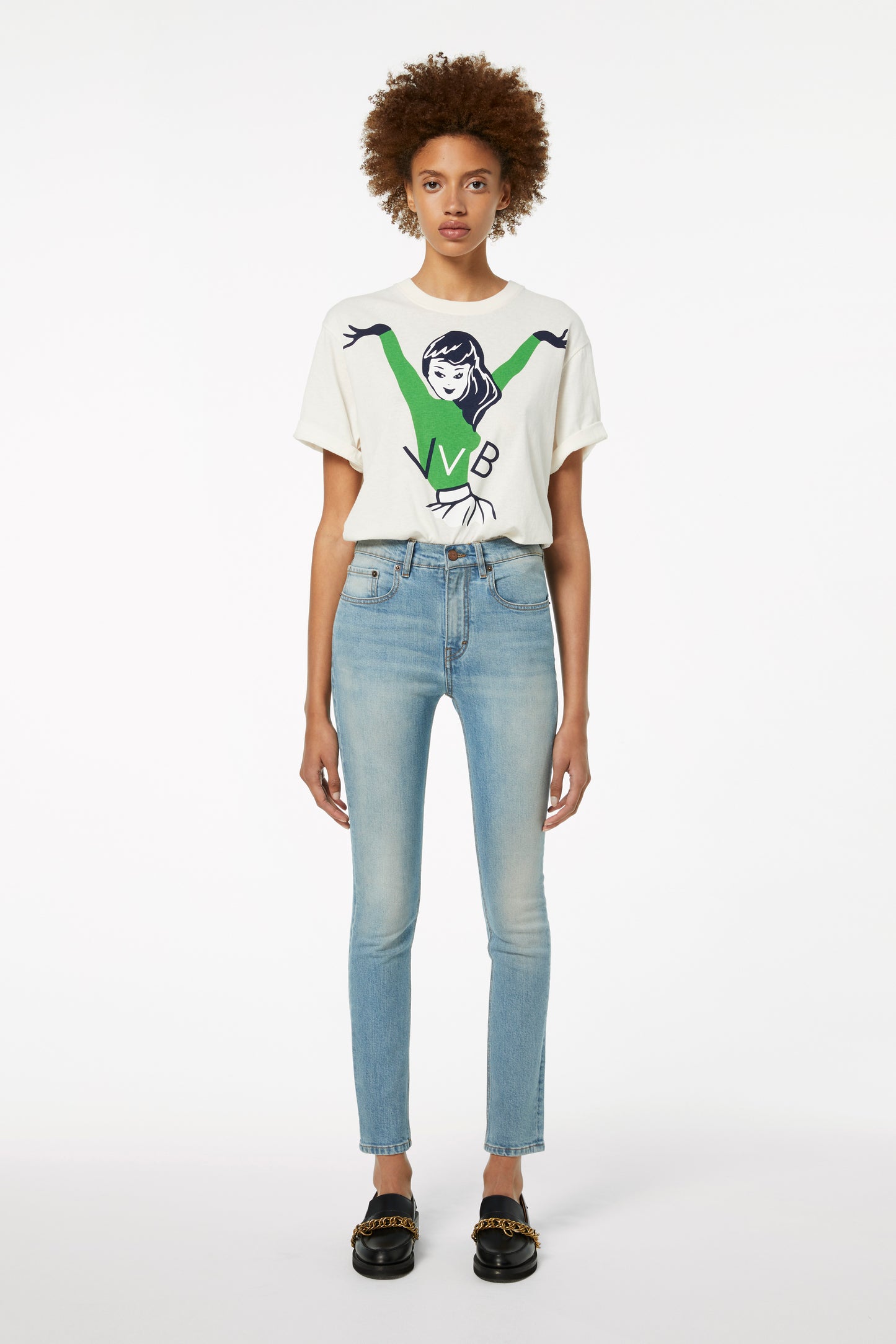 A person wearing a graphic t-shirt, Victoria Beckham's Cali Jeans in Parisian Blue, and black shoes stands against a plain white background.