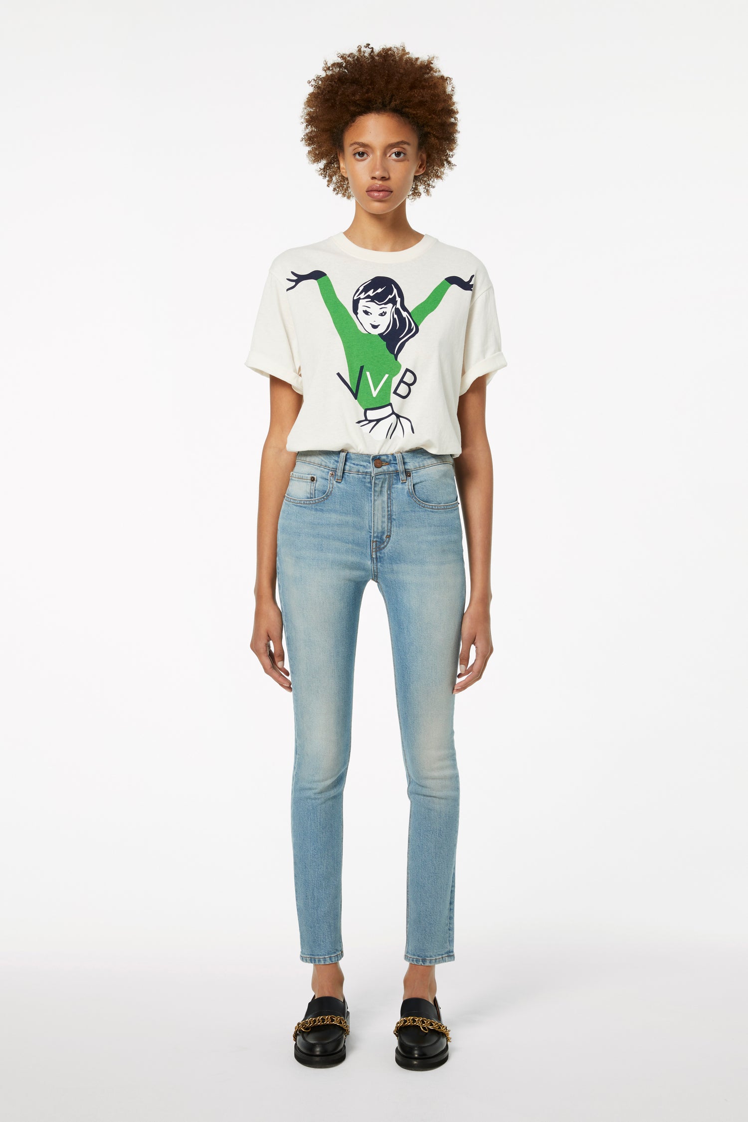 A person wearing a graphic t-shirt, Victoria Beckham's Cali Jeans in Parisian Blue, and black shoes stands against a plain white background.