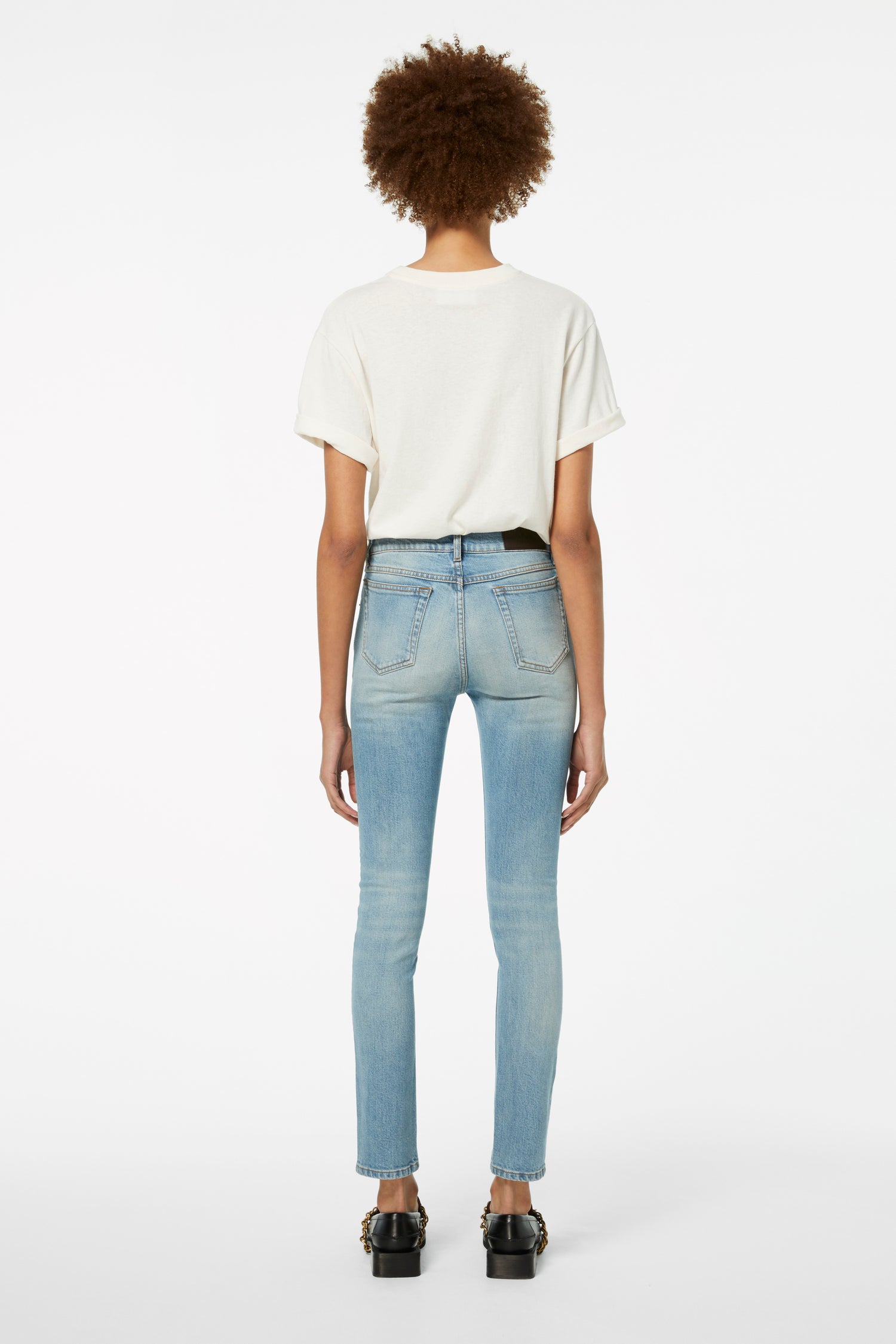 A person wearing a white shirt and Victoria Beckham's Cali Jeans in Parisian Blue stands against a plain white background, viewed from the back.