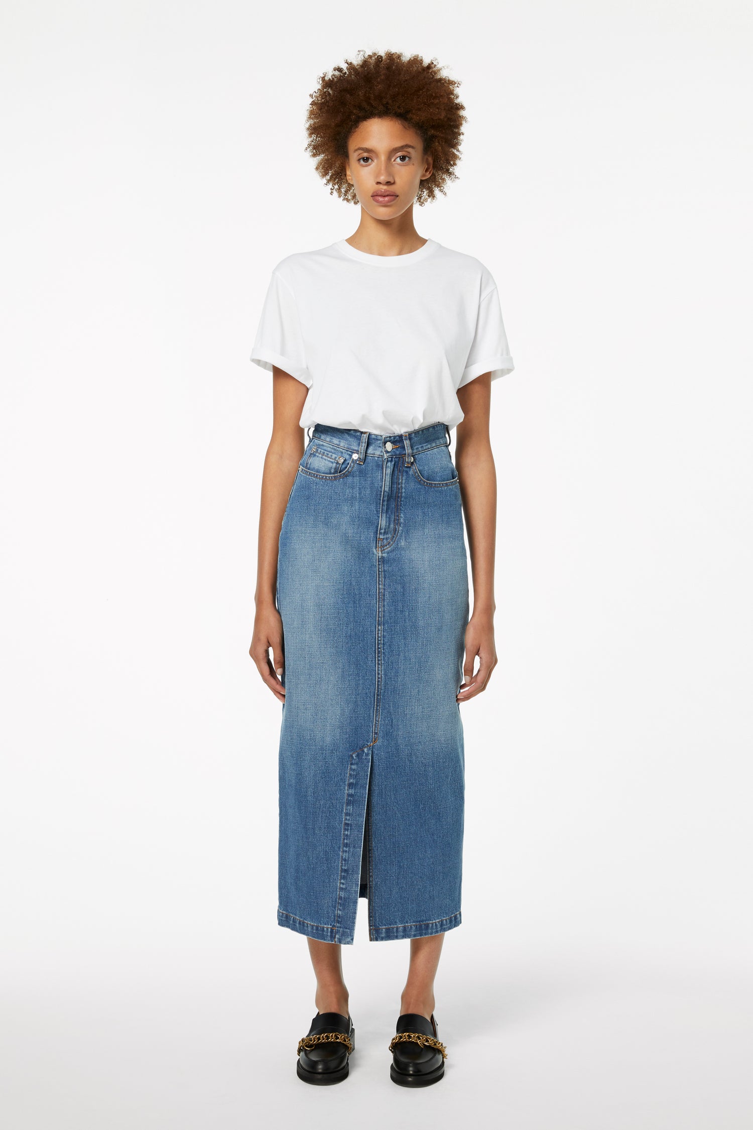 A person wearing a white t-shirt, Front Split Denim Midi Skirt in Fresh Blue by Victoria Beckham, and black shoes stands against a plain white background, showcasing a perfect transitional style.