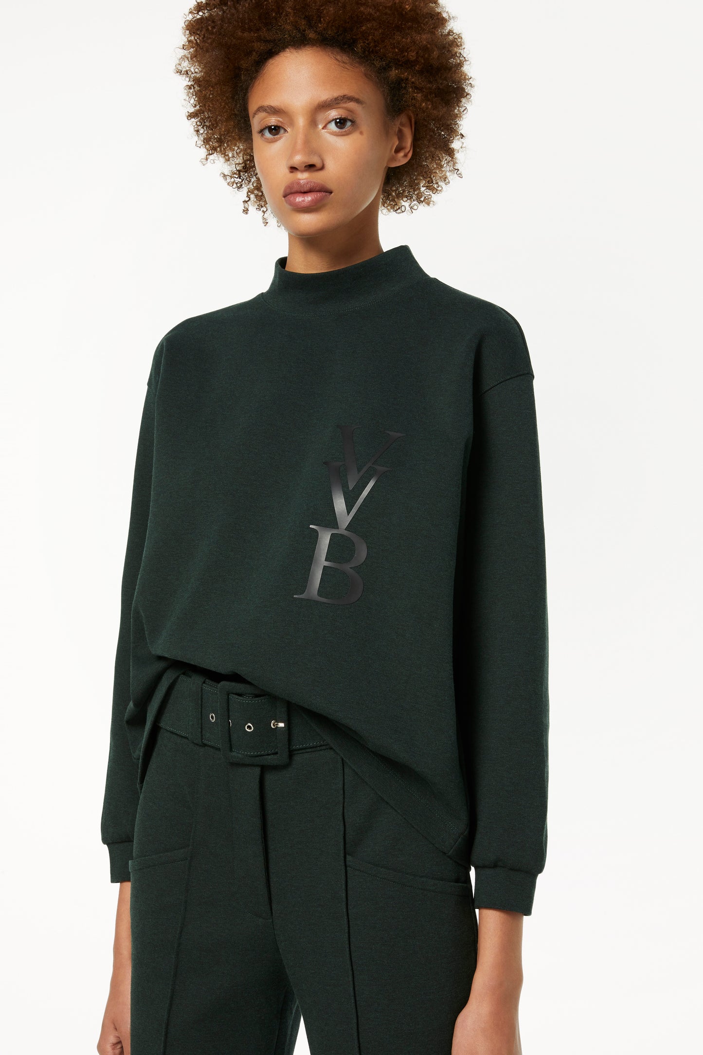 The woman is wearing a 3D Logo Sweatshirt in Ivy Green and matching trousers by Victoria Beckham.