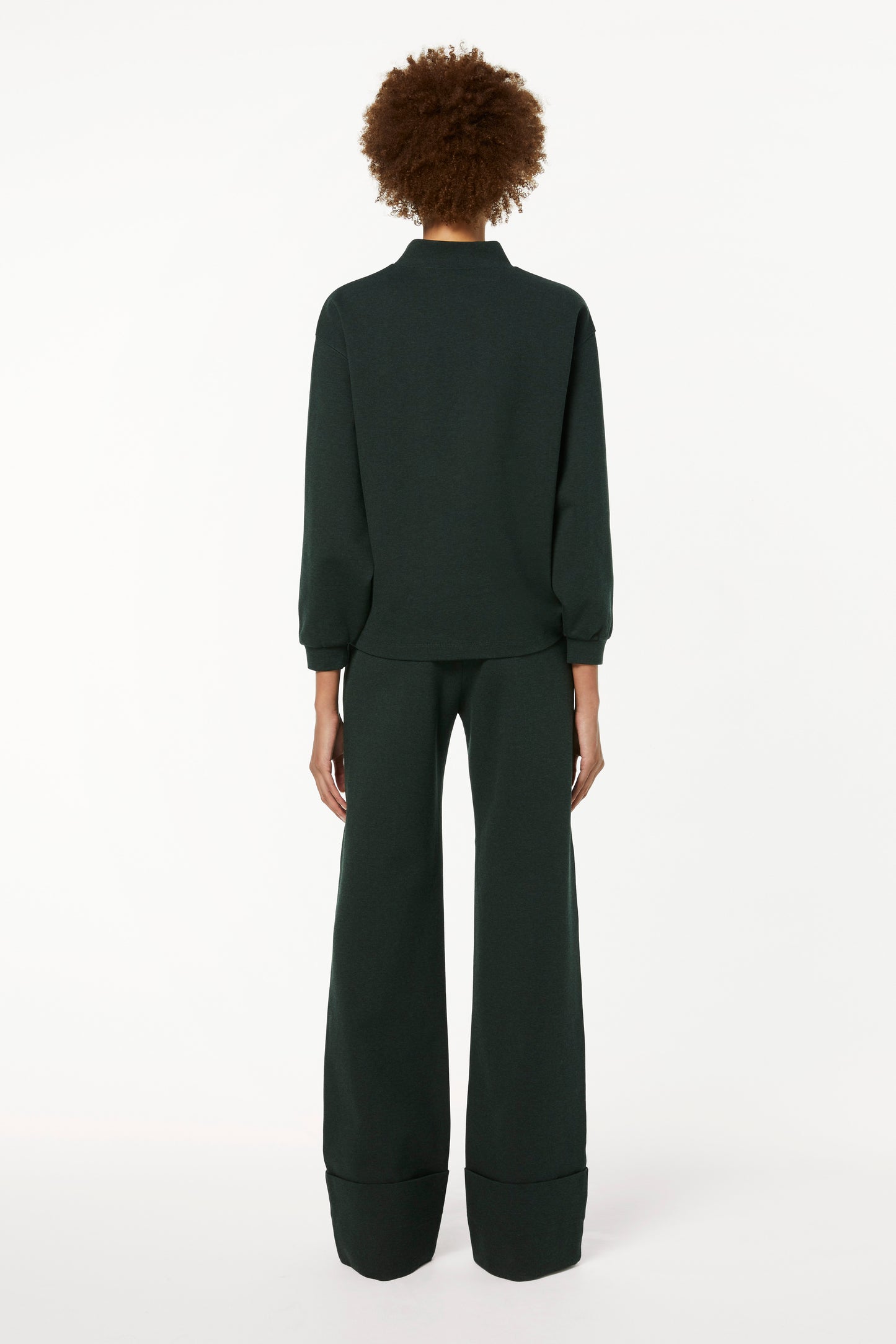 The back view of a woman wearing a Victoria Beckham 3D Logo Sweatshirt in Ivy Green and wide leg pants in loungewear styling.