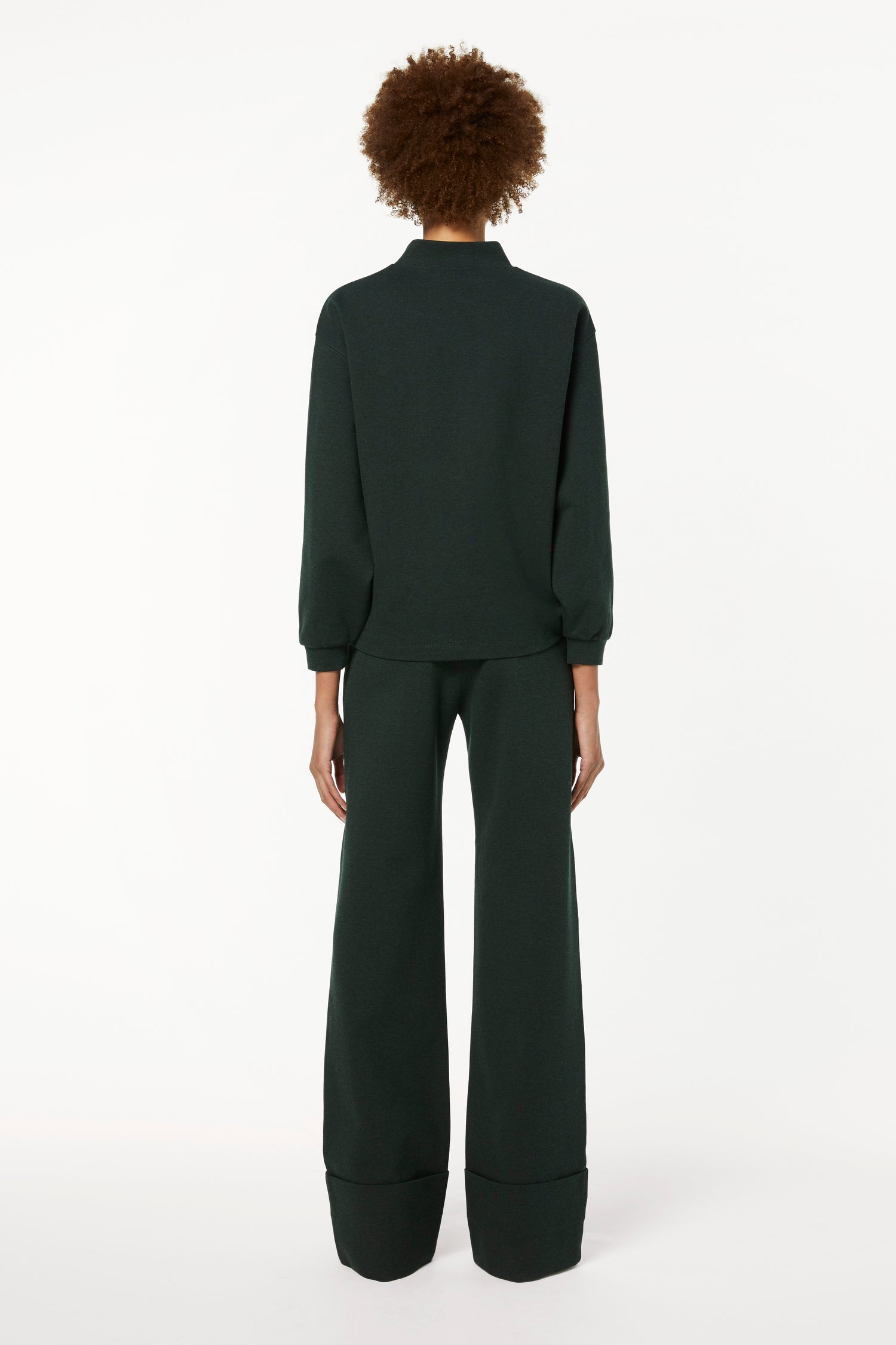 The back view of a woman wearing a Victoria Beckham 3D Logo Sweatshirt in Ivy Green and wide leg pants in loungewear styling.
