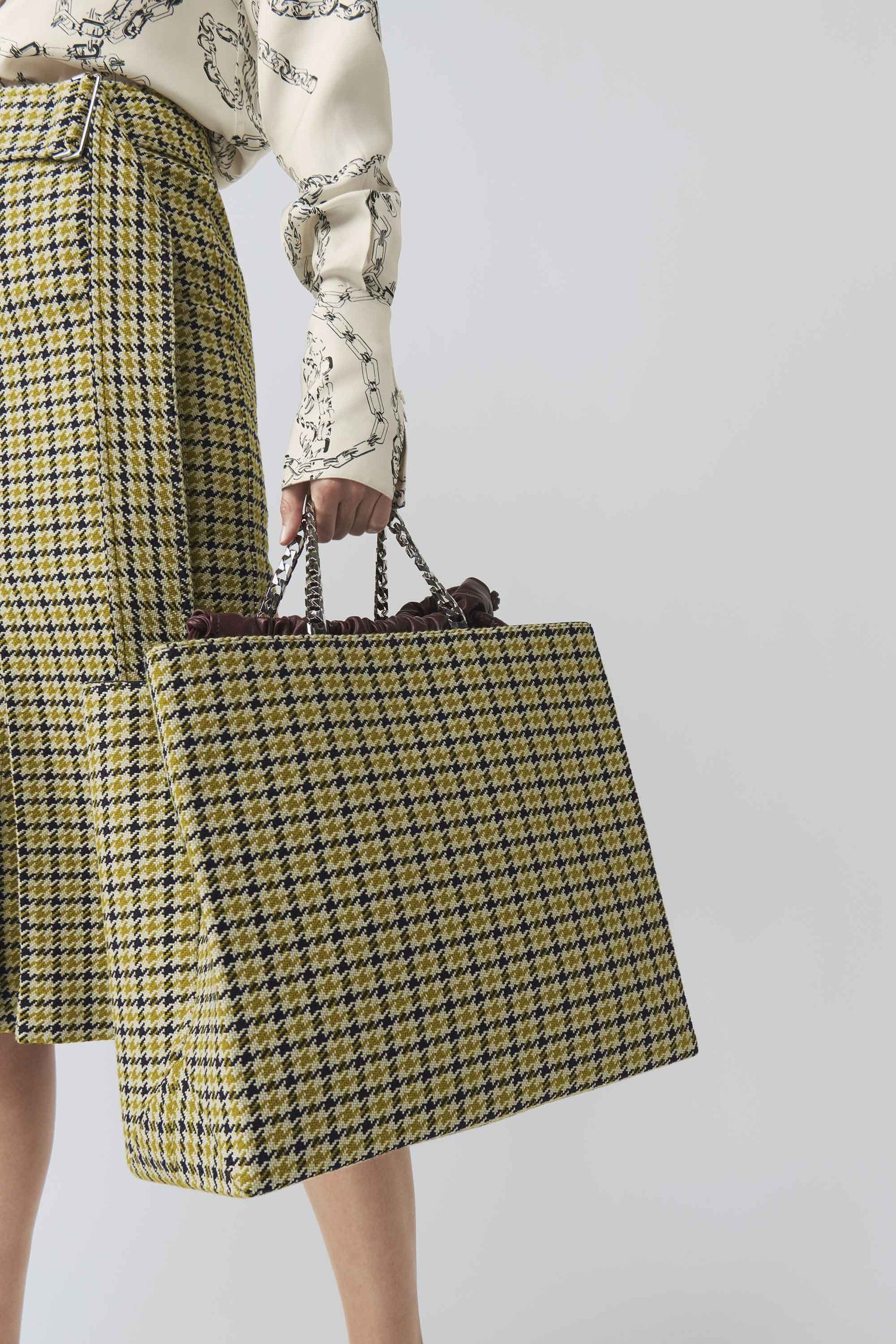 A woman wearing a yellow plaid skirt and carrying a Victoria Beckham 70's Collar Shirt bag.