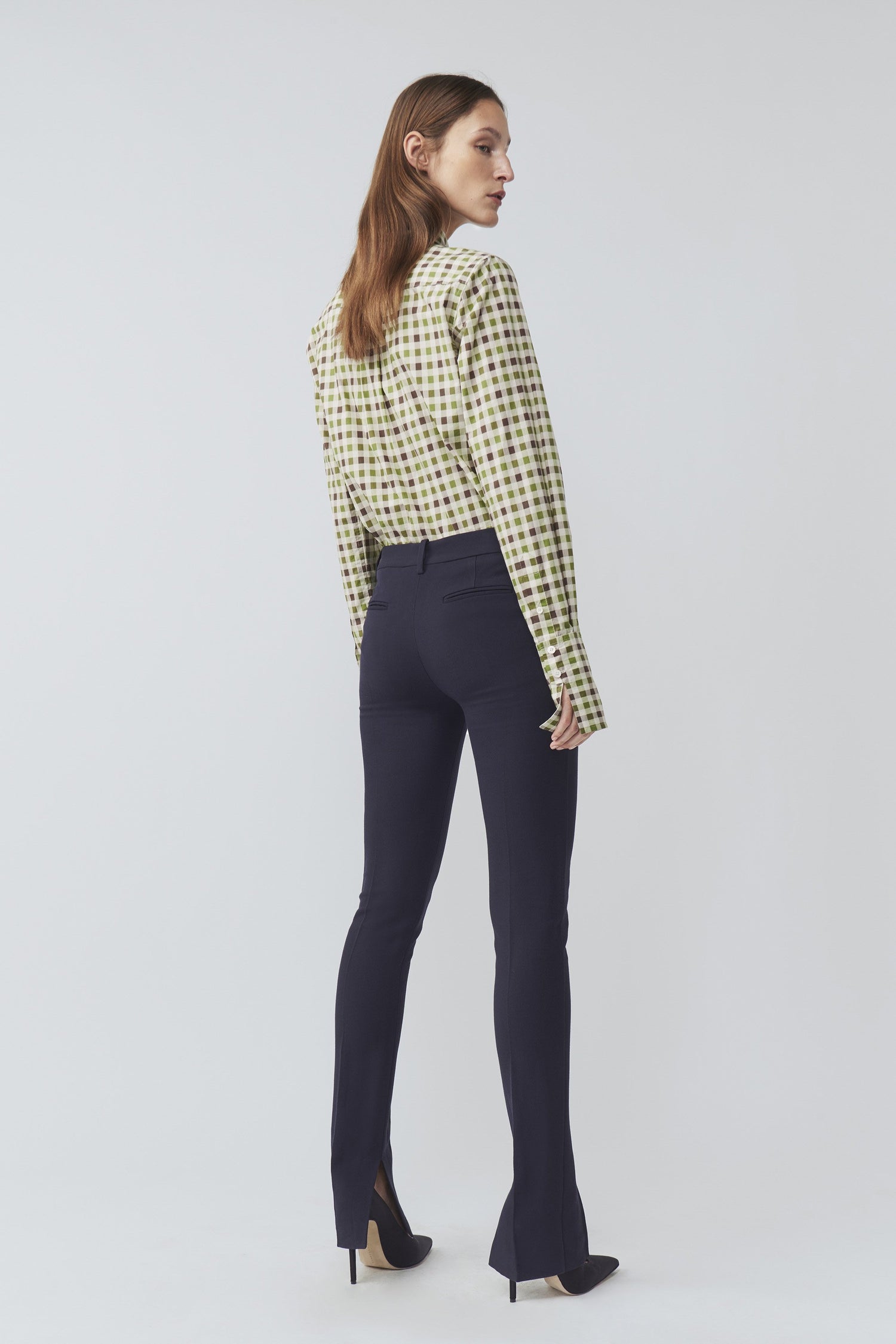 The back view of a woman wearing navy trousers and a 70's Collar Shirt with a point collar.