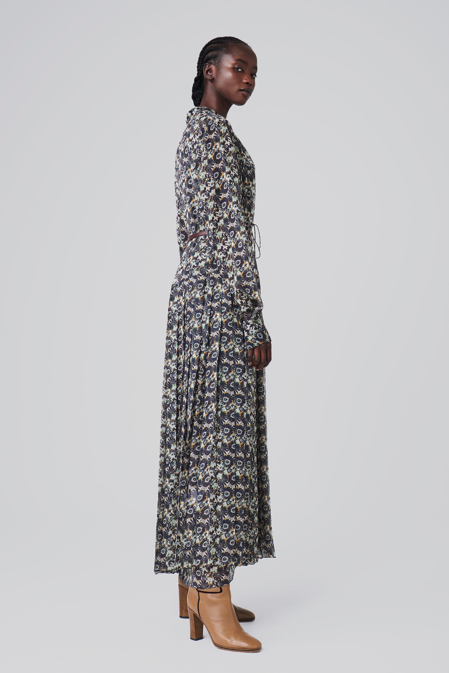 A person in a Victoria Beckham Pleated Dress in Navy Floral Print and tan boots stands in profile against a plain background.