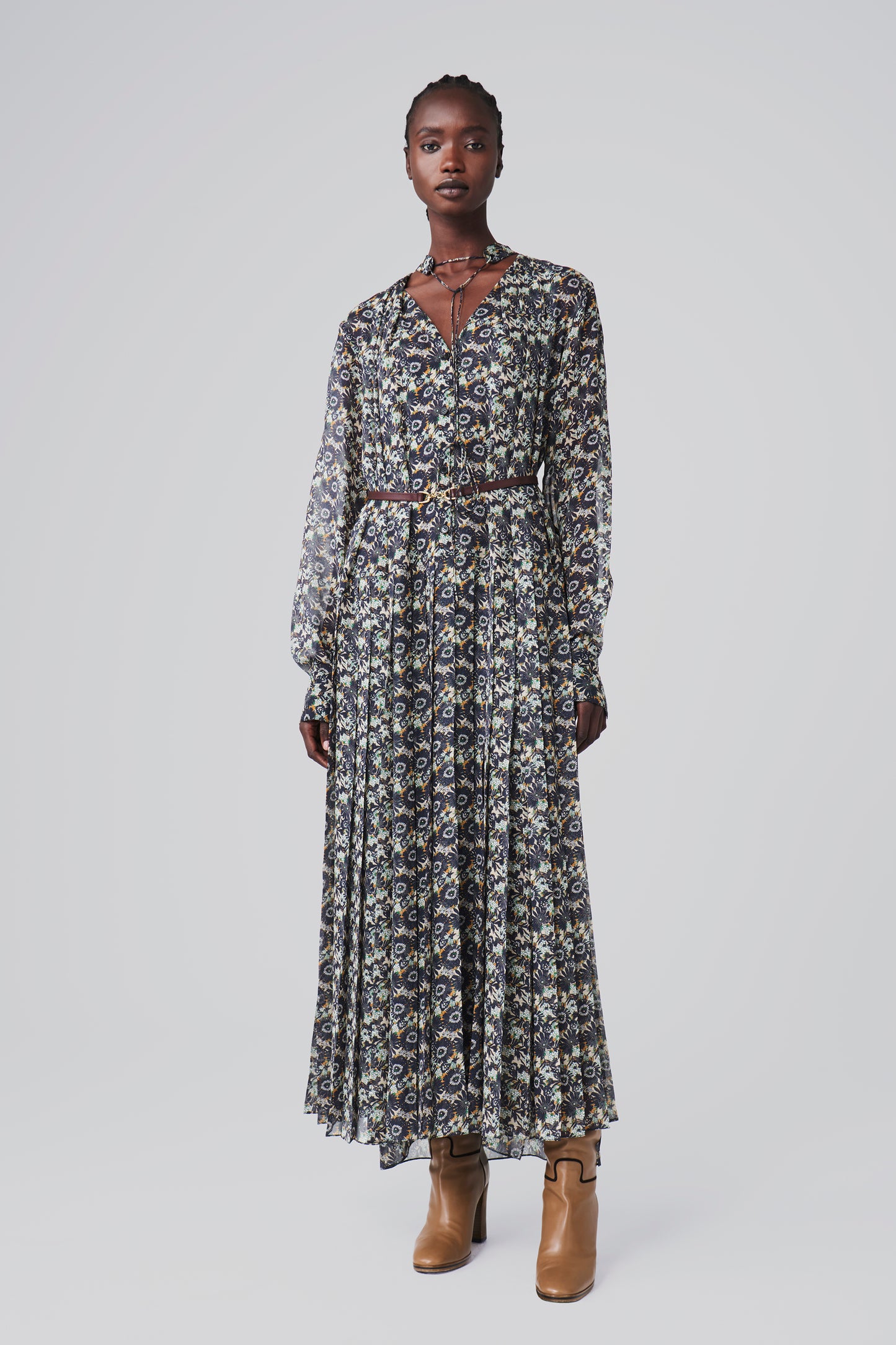 A person wears the Victoria Beckham Pleated Dress in Navy Floral Print with long sleeves, paired with ankle boots, against a plain background.