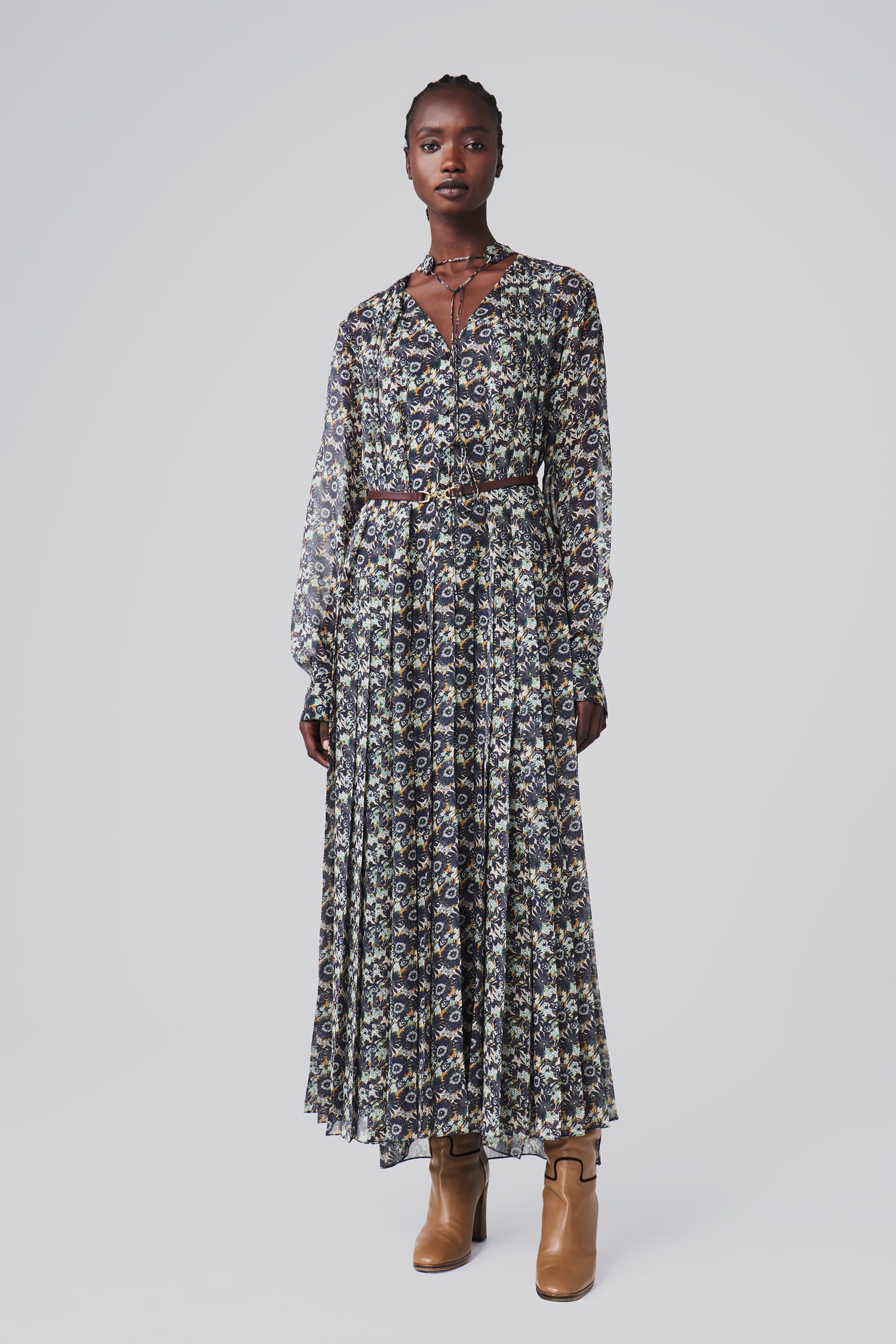 A person wears the Victoria Beckham Pleated Dress in Navy Floral Print with long sleeves, paired with ankle boots, against a plain background.