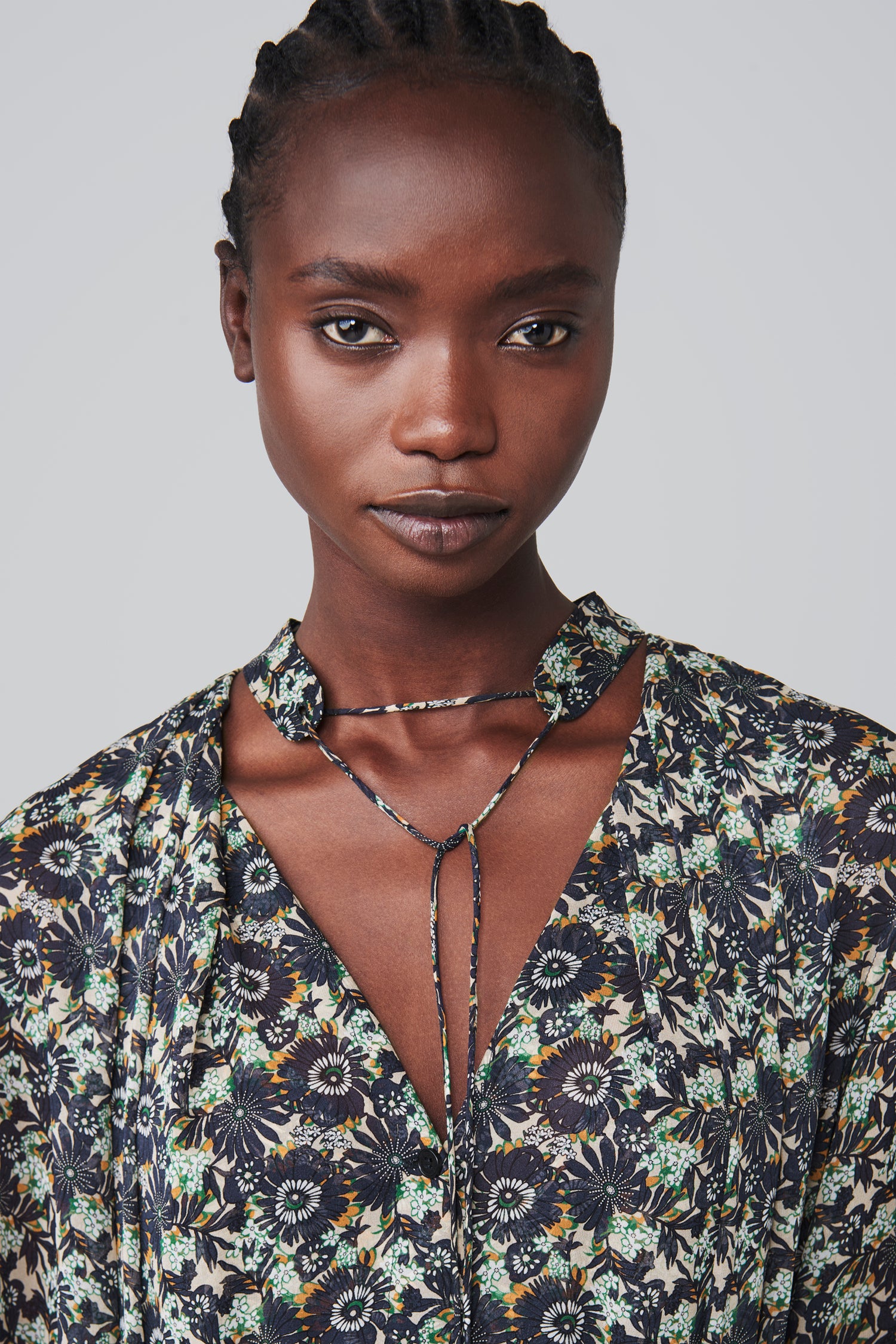 A person wearing a Victoria Beckham Pleated Dress in Navy Floral Print looks directly at the camera against a plain background.