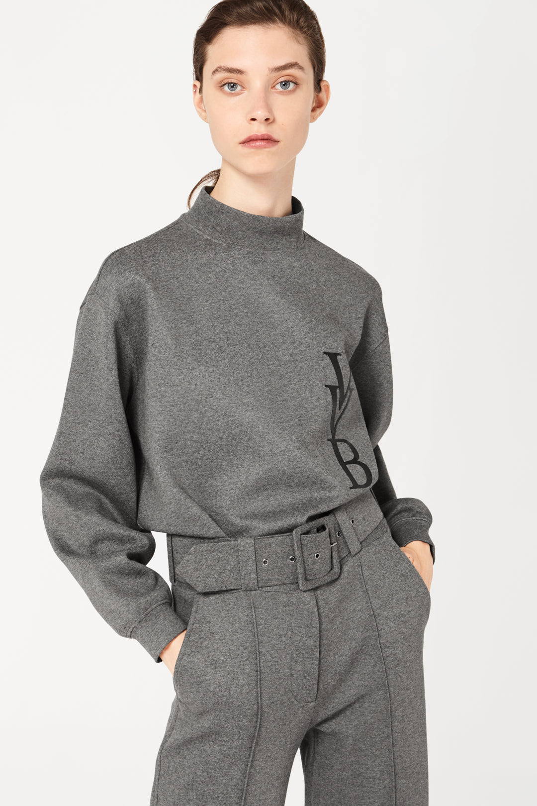 The model is wearing a Victoria Beckham 3D Logo Sweatshirt in Grey Melange and trousers.