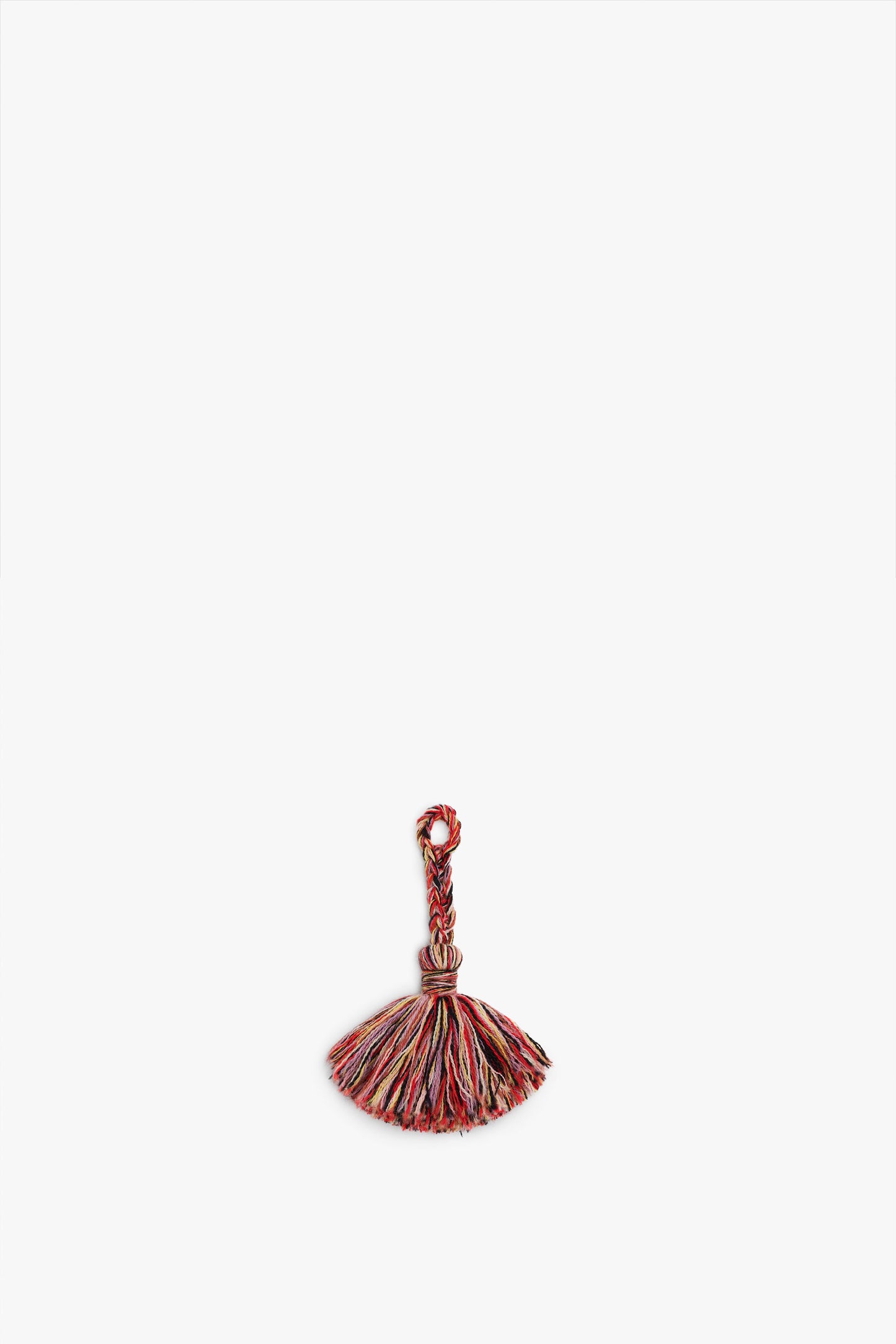 A small, multi-colored tassel made from merino wool yarn with a looped top and frayed bottom sits against a plain white background, created using the Victoria Beckham VB x Woolmark Crochet Keyring Kit.